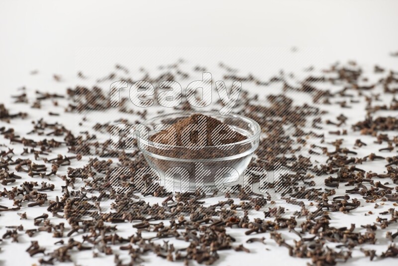 A glass bowl full of cloves powder and cloves grains spread on white flooring
