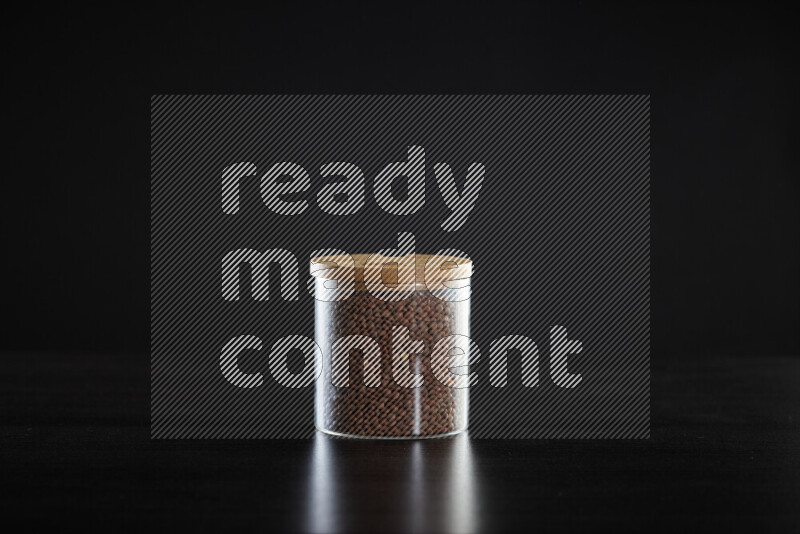 Brown lentils in a glass jar on black background