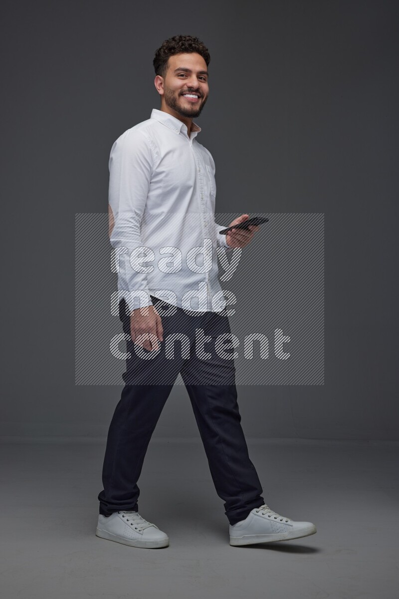 A man wearing smart casual standing and using his phone eye level on a gray background