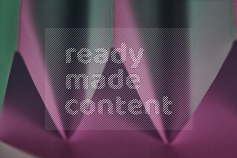 A close-up abstract image showing sharp geometric paper folds in green and pink gradients