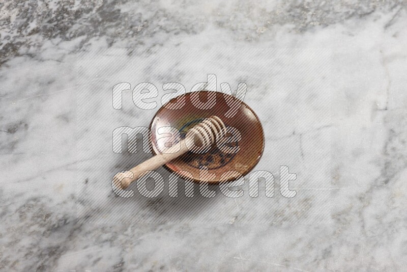 Decorative pottery plate with wooden honey dipper in it on grey marble background
