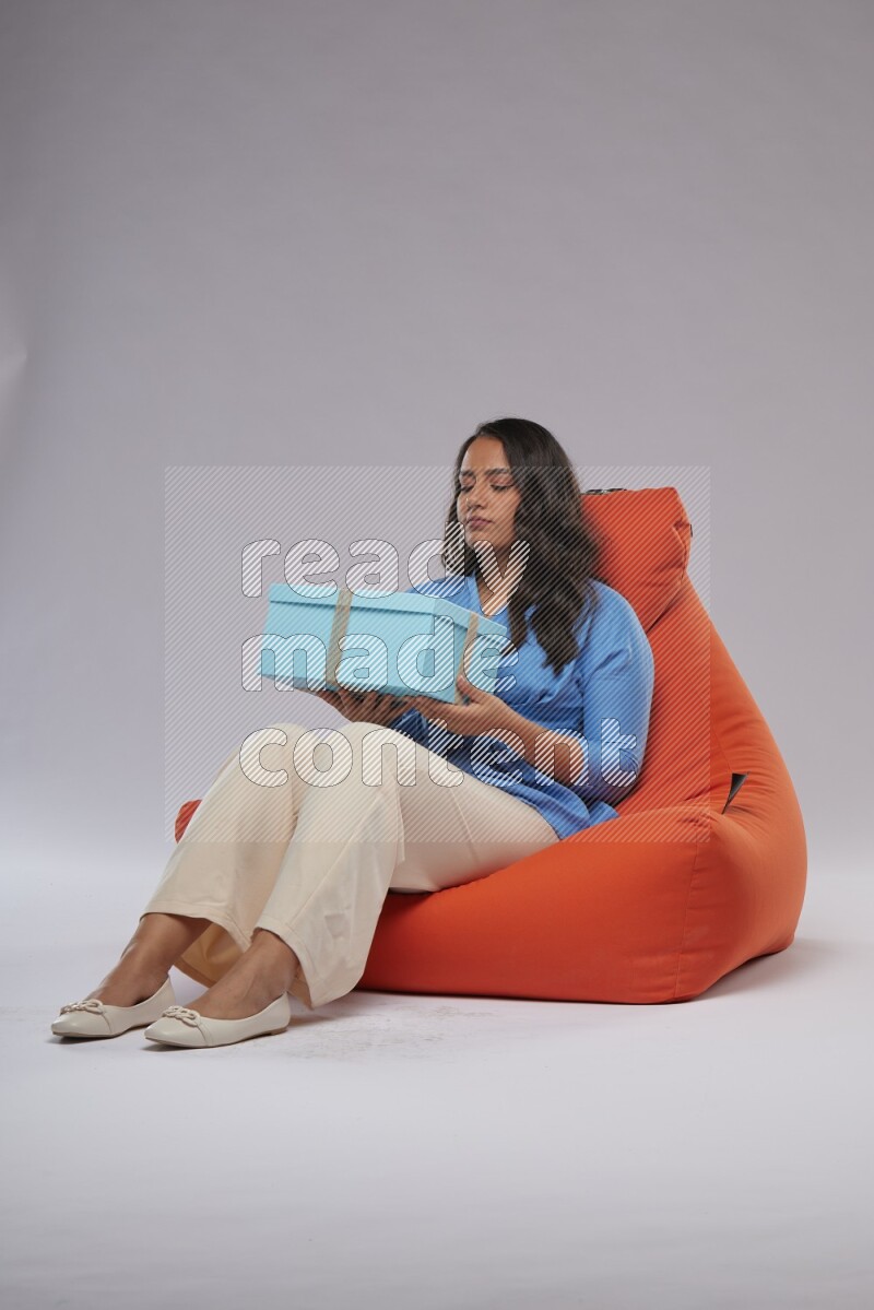 A woman sitting on an orange beanbag and opining a gift