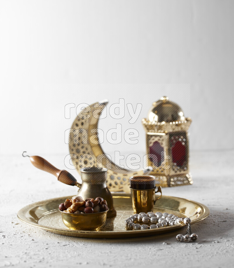 Nuts in a metal bowl with coffee and prayer beads on a tray beside lanterns in a light setup