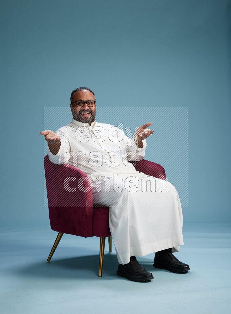 Saudi Man without shimag sitting on chair Interacting with the camera on blue background