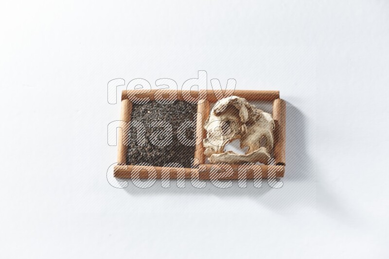 مربعان من أعواد القرفة ممتلئان بالشاي الأسود والزنجبيل المجفف علي خلفية بيضاء