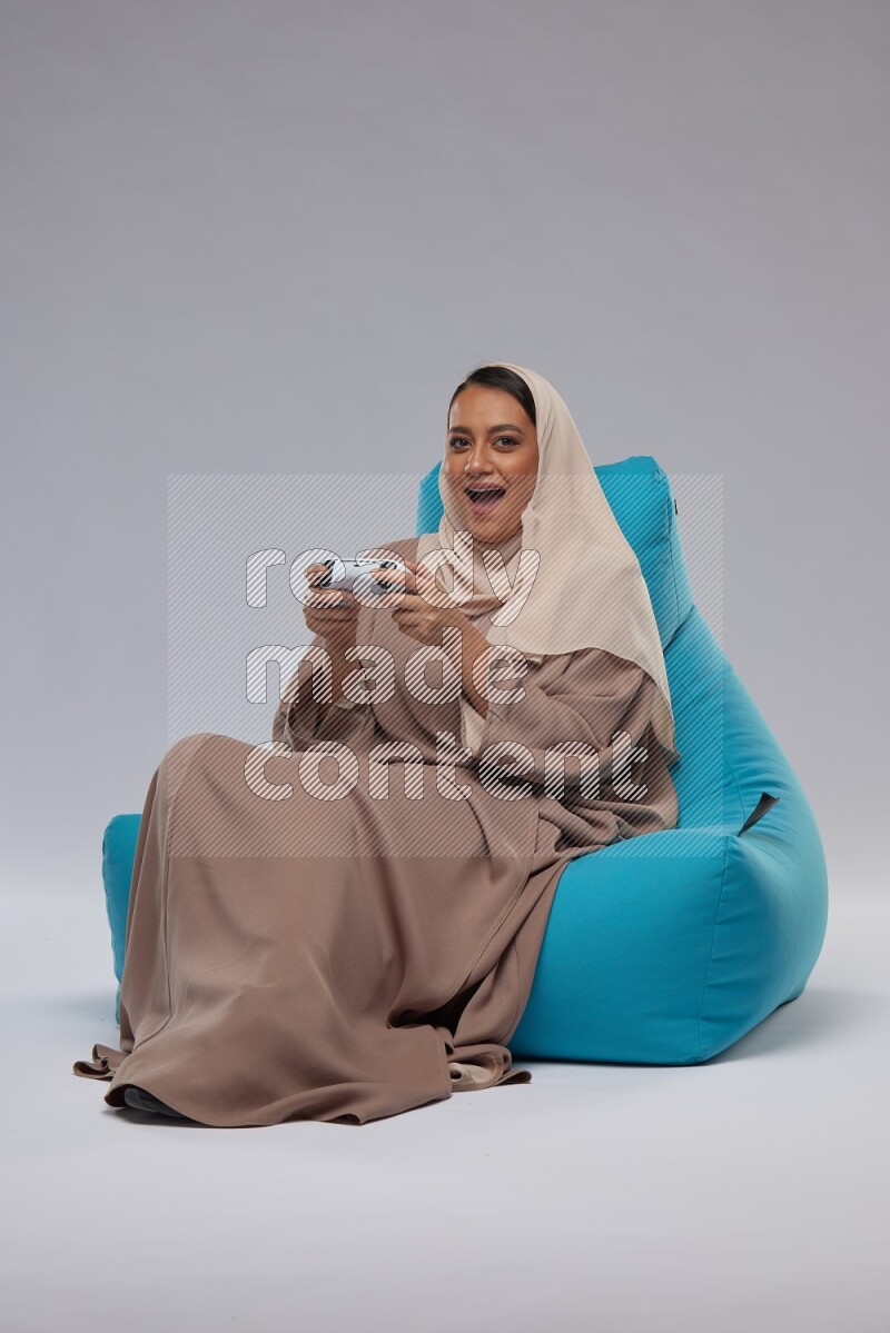 A Saudi woman sitting on a blue beanbag and gaming with joystick