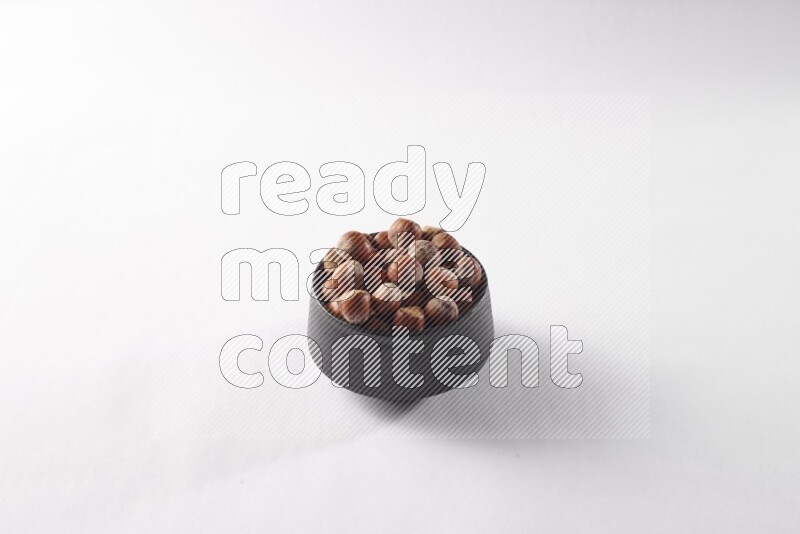 Hazelnuts in a black pottery bowl on white background