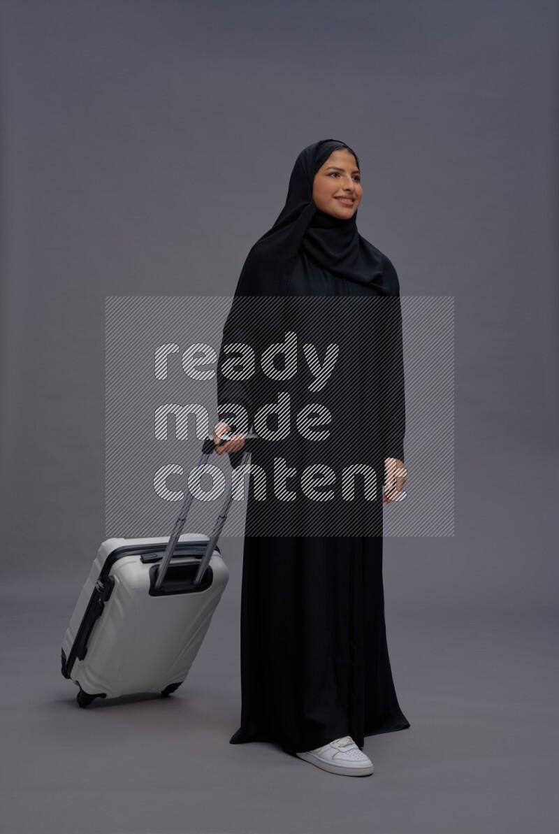 Saudi woman wearing Abaya standing holding bag on gray background