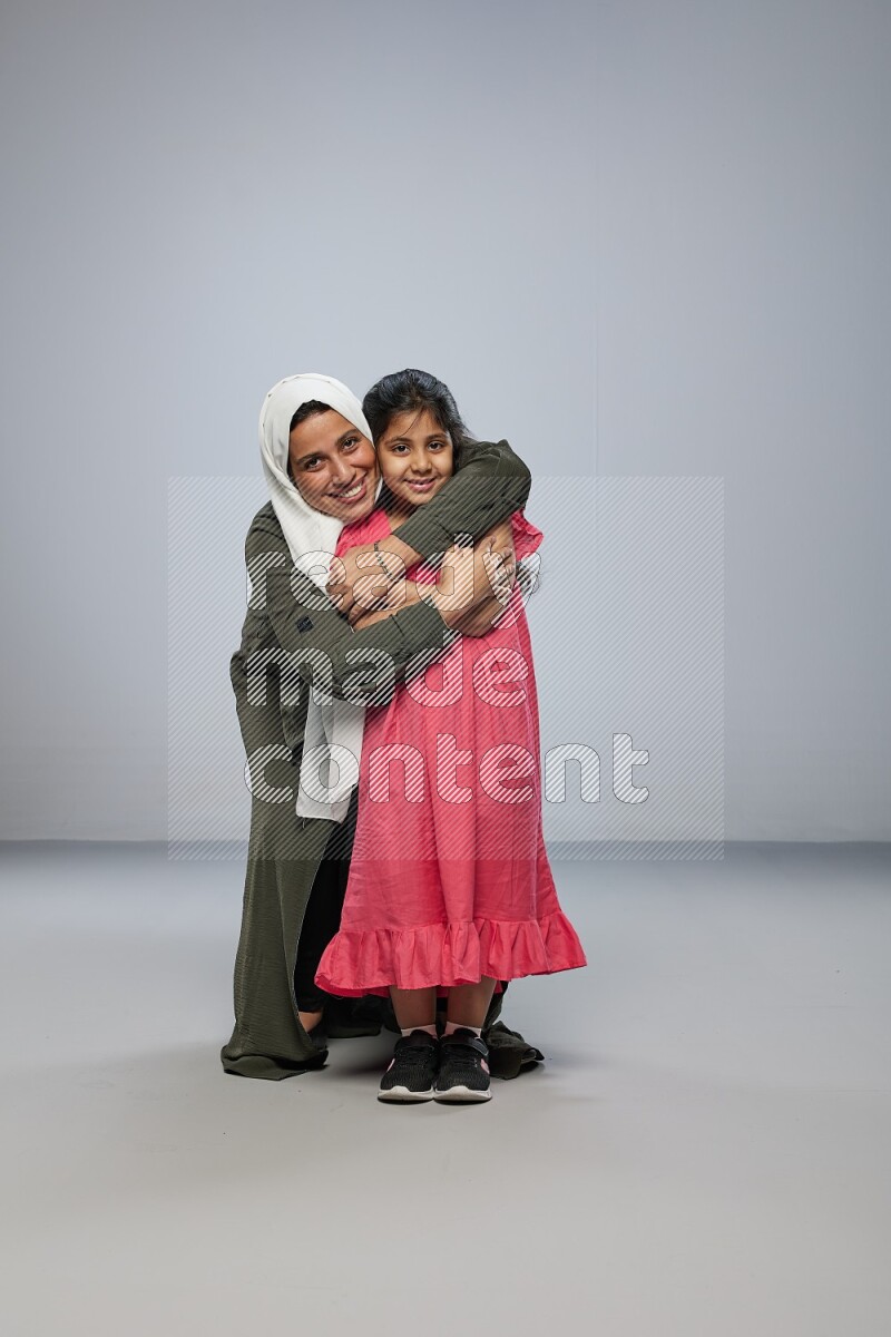 A girl and her mother interacting with the camera on gray background