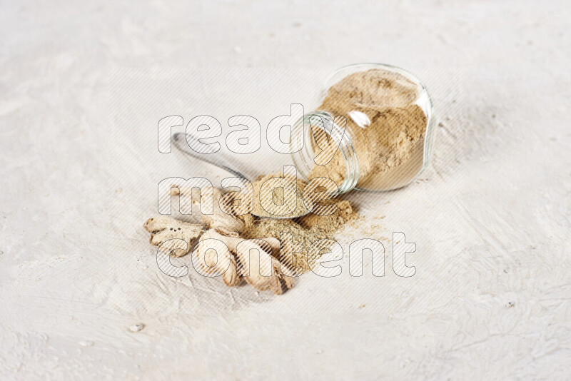 A glass jar full of ground ginger powder flipped with some spilling powder on white background
