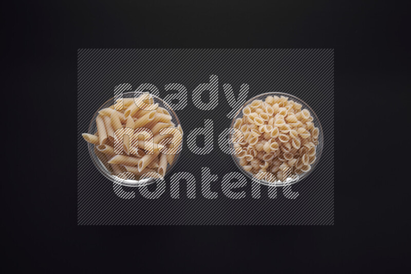 Different pasta types in glass bowls on black background