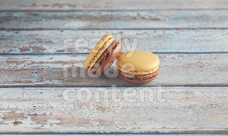 45º Shot of two Yellow and Brown Chai Latte macarons on light blue wooden background