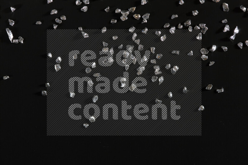 Silver shimmering fragments of glass scattered on a black background