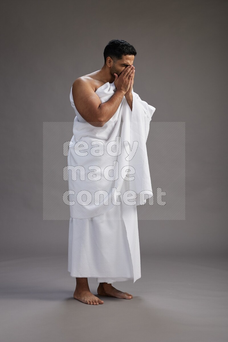 A man wearing Ehram standing showing how to sneeze on gray background
