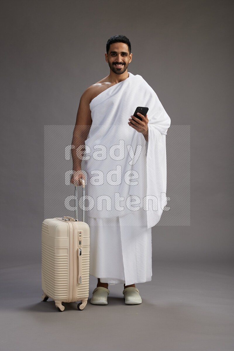 A man wearing Ehram Standing holding traveling bag on gray background