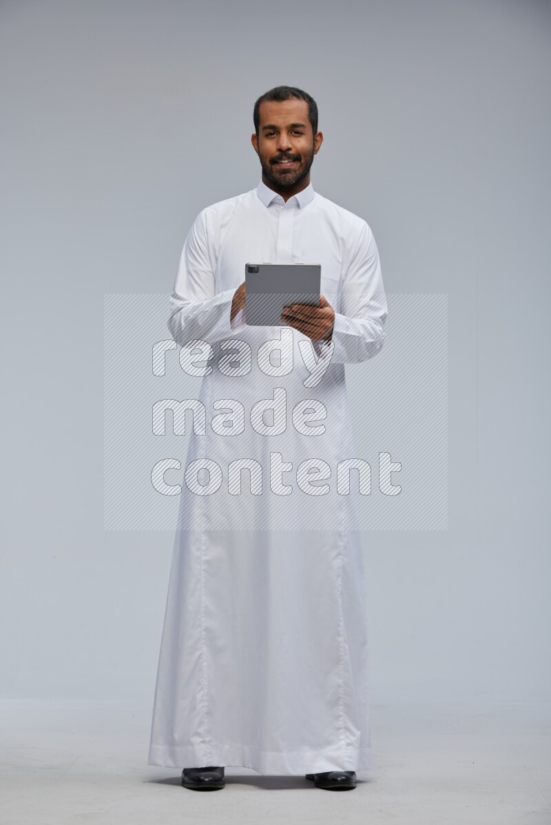 Saudi man wearing Thob standing working on tablet on Gray background