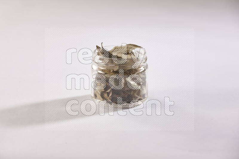 A glass jar filled with dried bay leaves on white flooring
