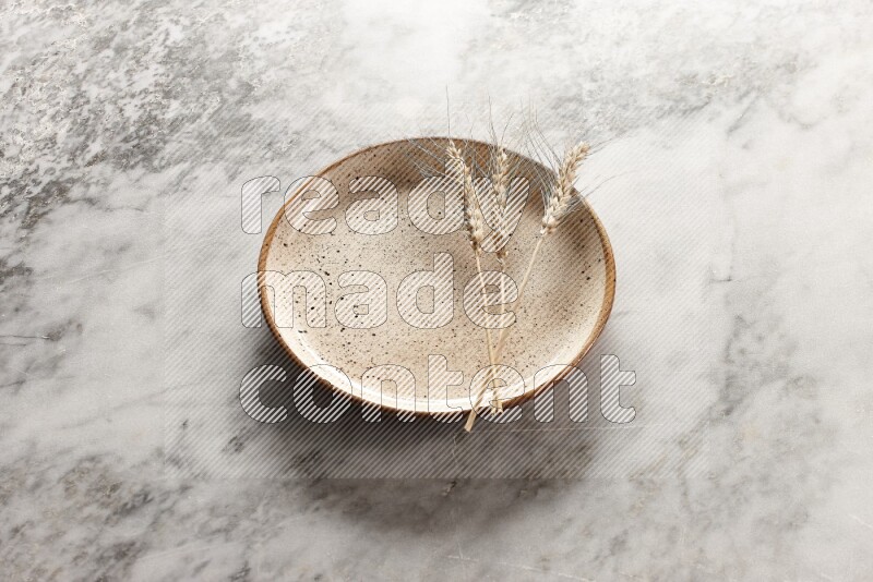 Wheat stalks on multicolored pottery plate on grey marble background