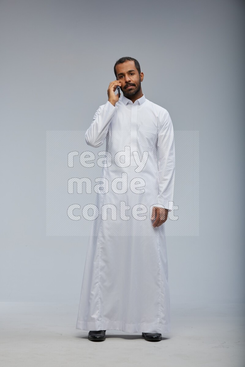 Saudi man wearing Thob standing talking on phone on Gray background