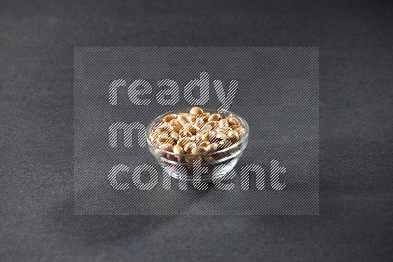 A glass bowl full of peeled peanuts on a black background in different angles