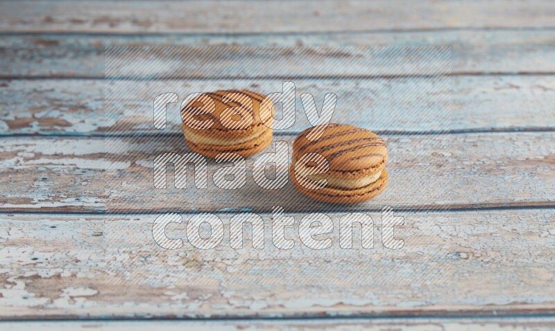 45º Shot of two light brown Almond Cream macarons on light blue wooden background