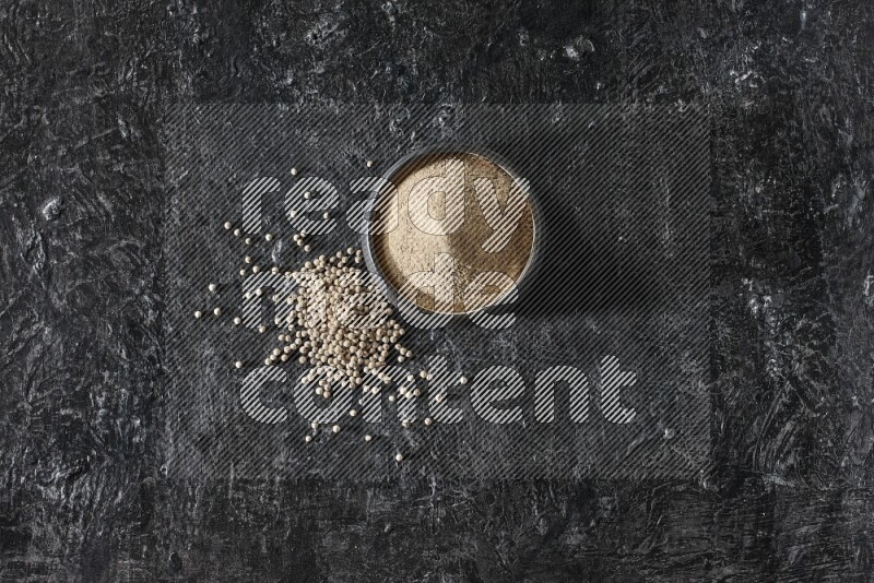 وعاء فخار أسود مملوء ببودرة الفلفل الأبيض مع حبات الفلفل الأبيض على أرضية سوداء