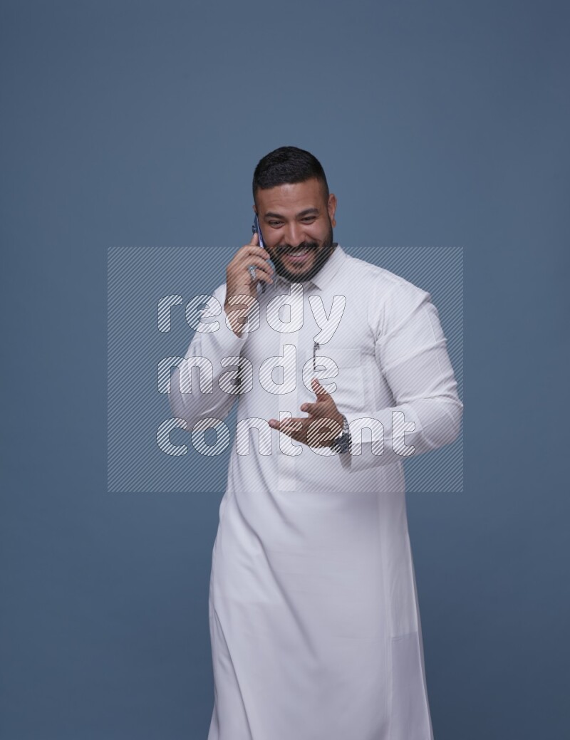 A Saudi man calling on blue background wearing Saudi Thob