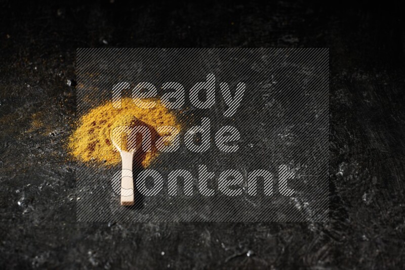 ملعقة خشبية ممتلئة ببودرة الكركم على خلفية سوداء