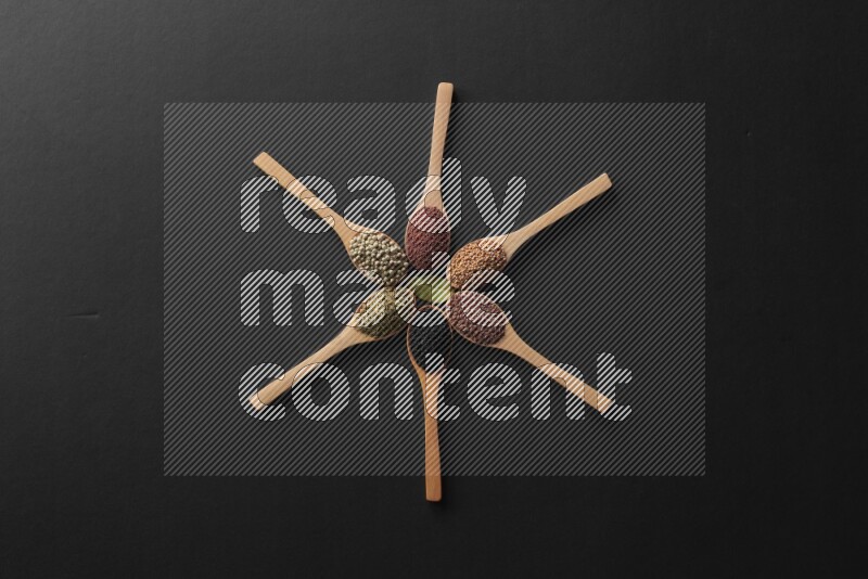 الفلفل الأسود وحبوب الخردل وحبة البركة وحب الرشاد والكمون و حبوب الكتان في معالق خشبية علي شكل ساعة علي خلفية سوداء