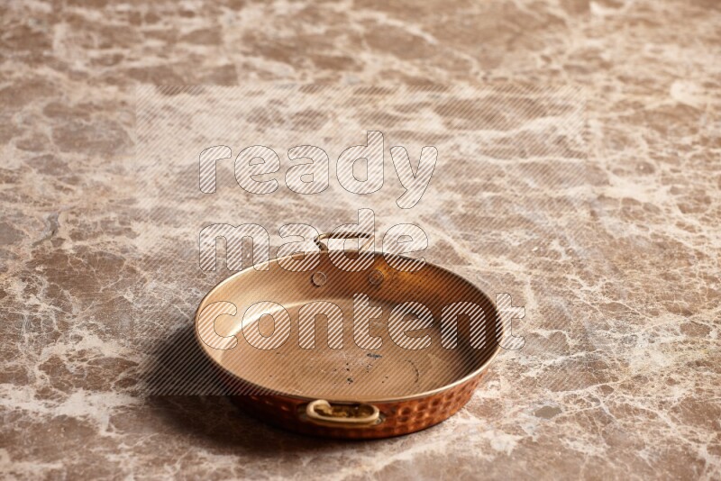 A small copper pan on beige marble background