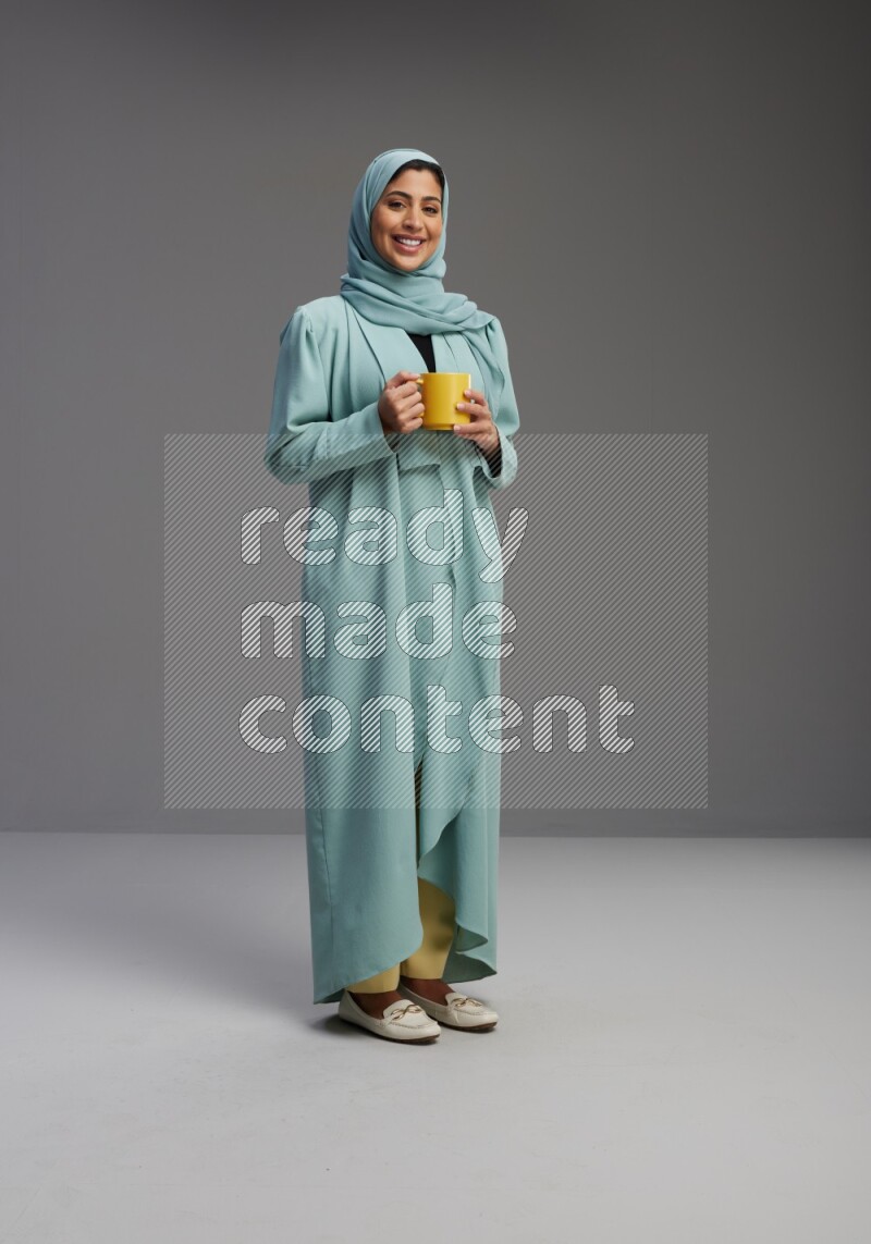 Saudi Woman wearing Abaya standing  holding a mug on Gray background