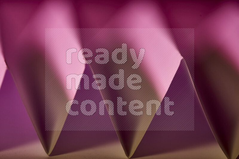 A close-up abstract image showing sharp geometric paper folds in pink gradients and warm tones