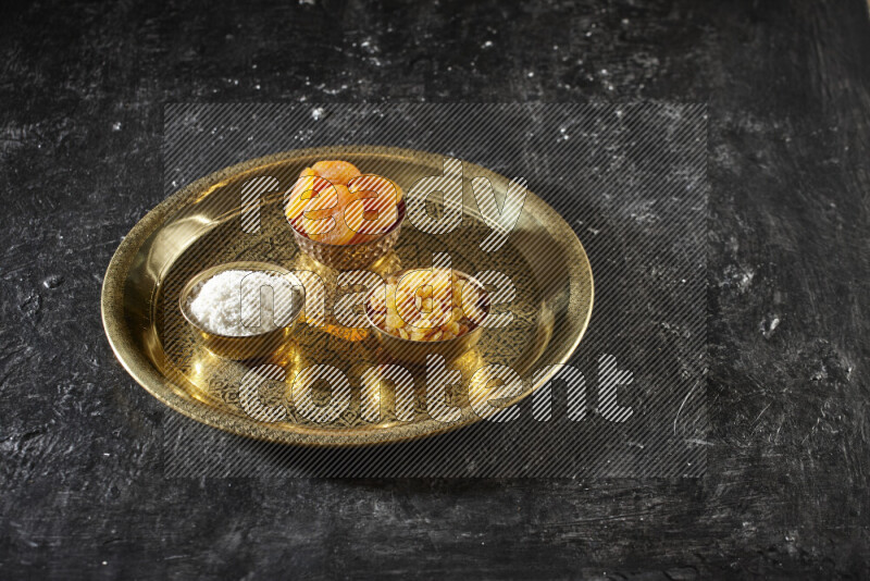 Dried fruits in metal bowls on a tray in a dark setup