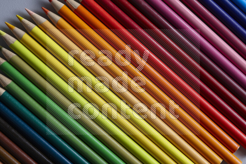 A collection of colored pencils arranged showcasing a gradient of different hues on grey background