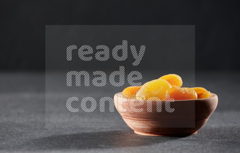 A wooden bowl full of dried apricots on a black background in different angles