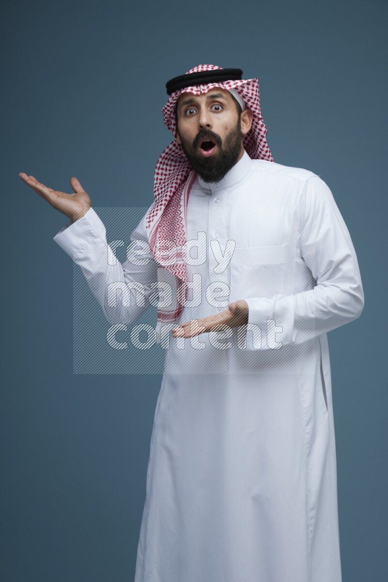 A man pointing in a blue background wearing Saudi Thob and Shomag