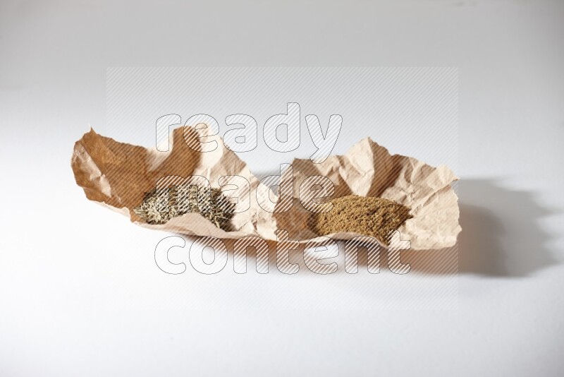 Cumin seeds and cumin powder in 2 crumpled pieces of paper on white flooring
