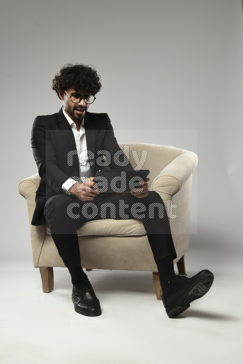 A man wearing formal sitting on a chair gaming on a tablet on white background