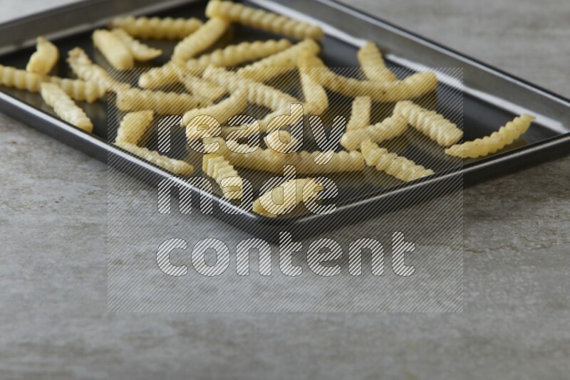 crinkle fries in a black stainless steel rectangle tray on grey textured counter top