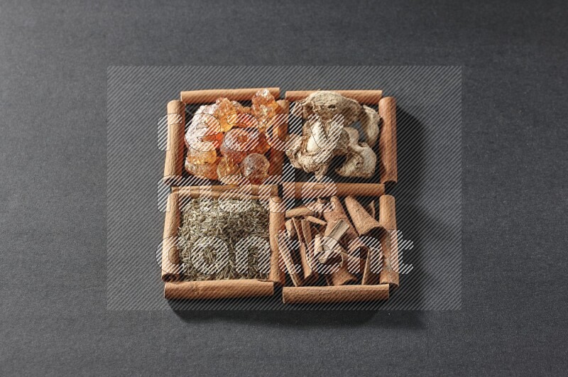 4 مربعات من عيدان القرفة ممتلئة بالصمغ العربي والزنجبيل المجفف وقطع القرفة والكمون على أرضية سوداء