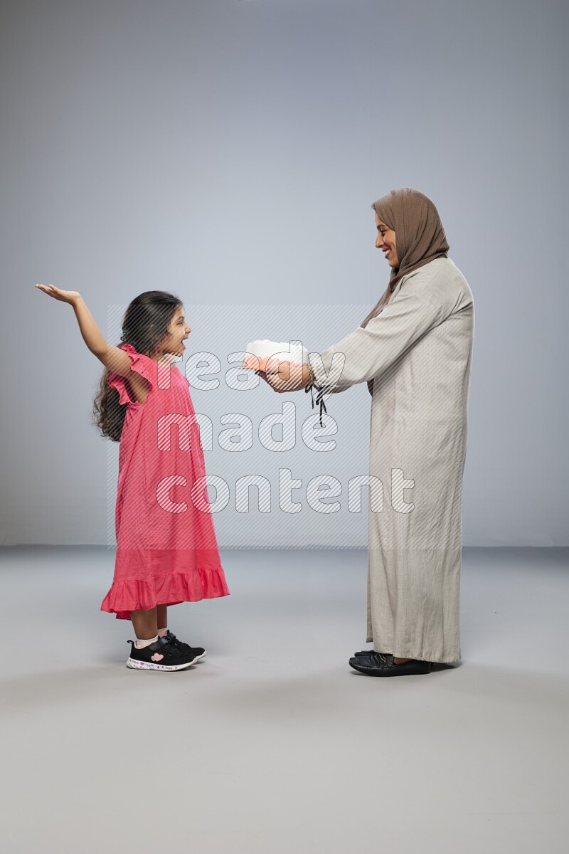 A mother giving a cake to her daughter on gray background