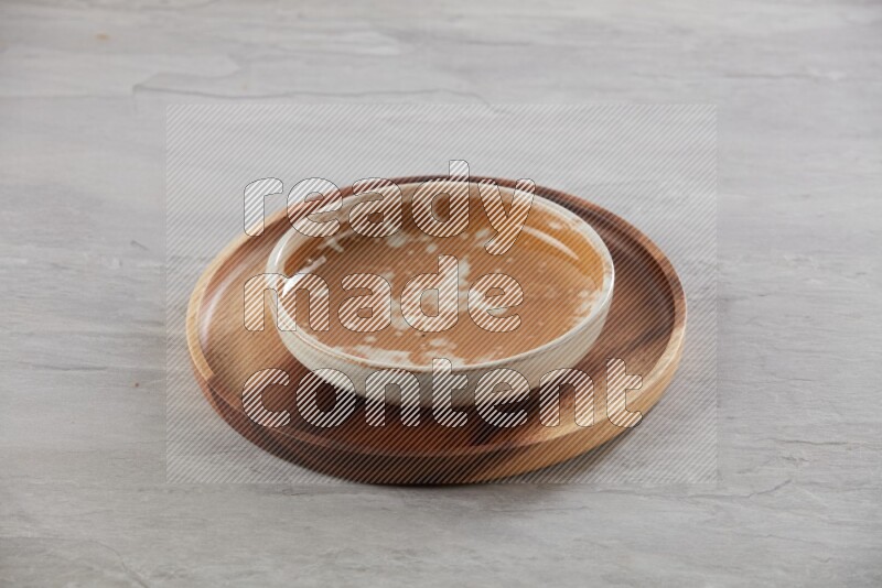 multi color pottery round dish on top of brown wood round plate and spoon, on grey textured countertop