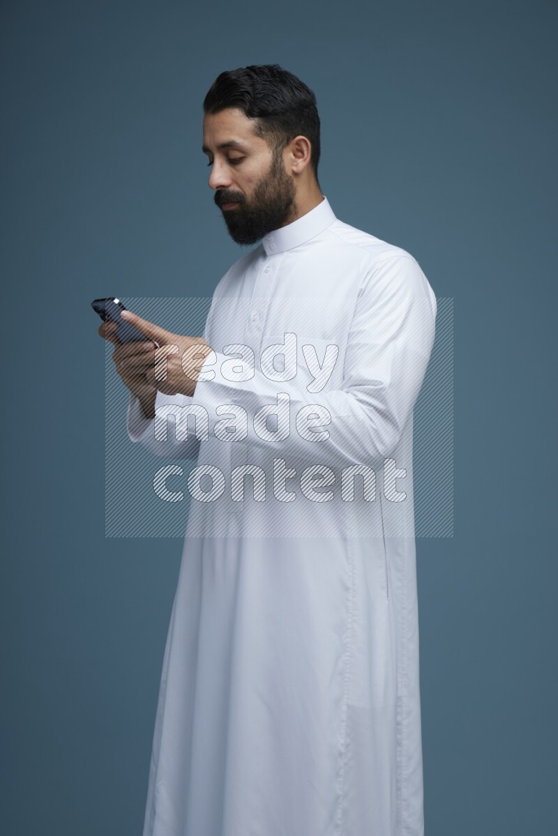 A man Texting in a blue background wearing Saudi Thob