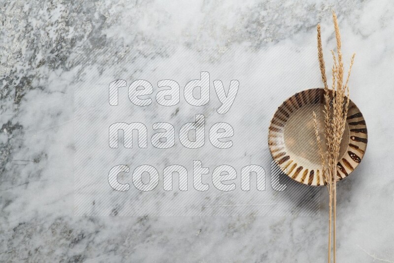 Wheat stalks on multicolored pottery plate on grey marble background