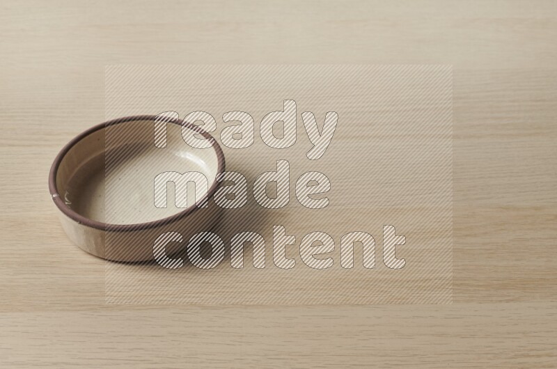 A beige pottery oven bowl on light wooden background
