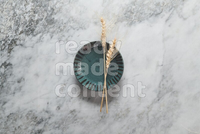 Wheat stalks on multicolored pottery plate on grey marble background