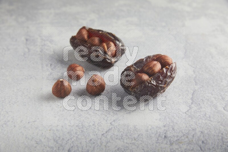 two hazelnuts stuffed madjoul dates on a light grey background
