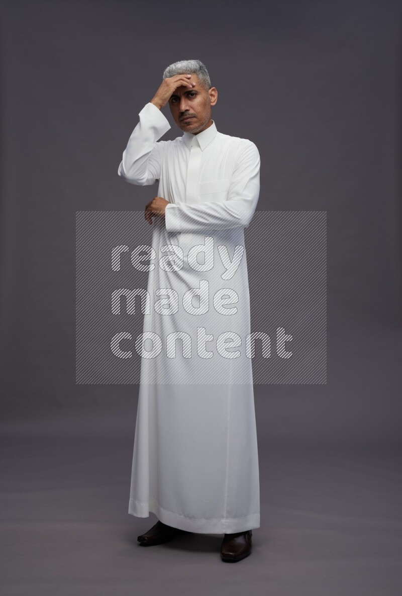 Saudi man wearing thob standing interacting with the camera on gray background