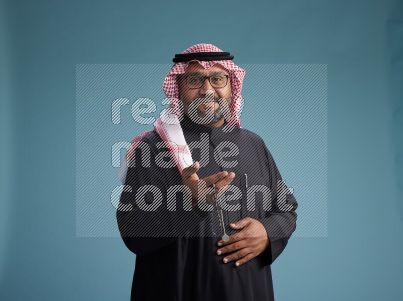 Saudi Man with shimag Standing Interacting with the camera on blue background