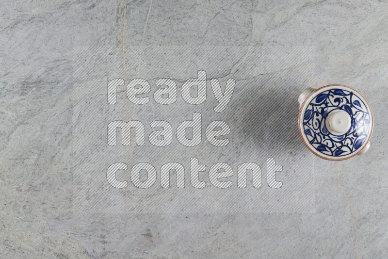 A multicolored pottery pot with its lid on grey marble background